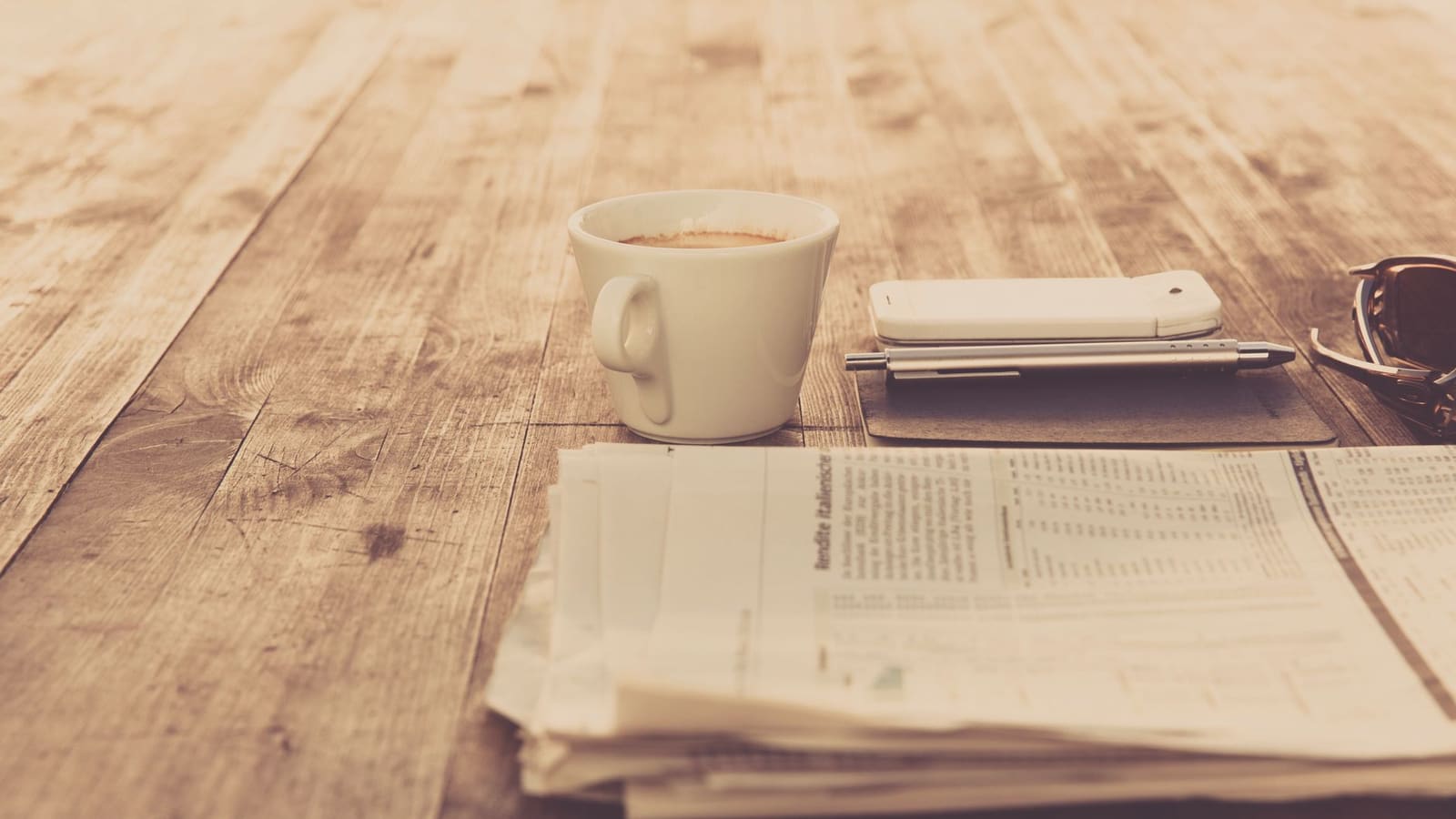 Una tazza di caffè accanto al giornale del mattino, su un tavolo di legno