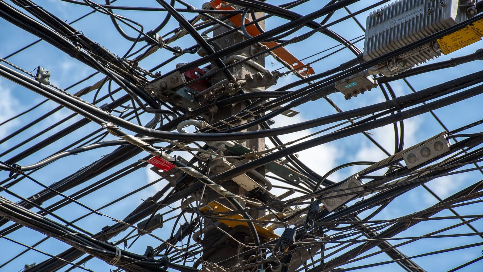 Un groviglio di cavi elettrici su un palo della luce, contro il cielo